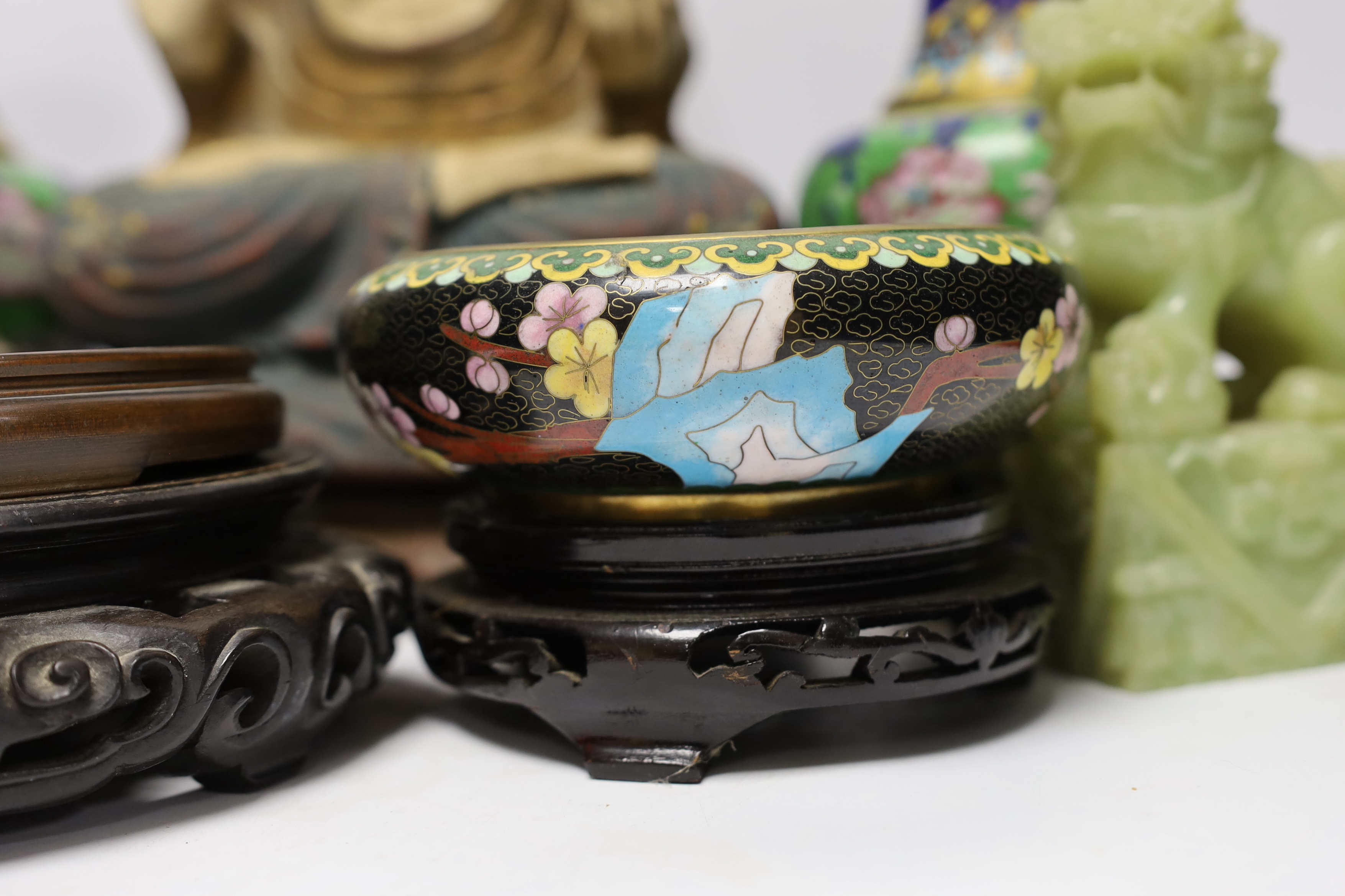 A pair of Chinese cloisonné enamel vases and a bowl on stand, two soap stone lion dogs, a carved and painted Buddha, a deity and four wooden stands, Buddha 33cm high